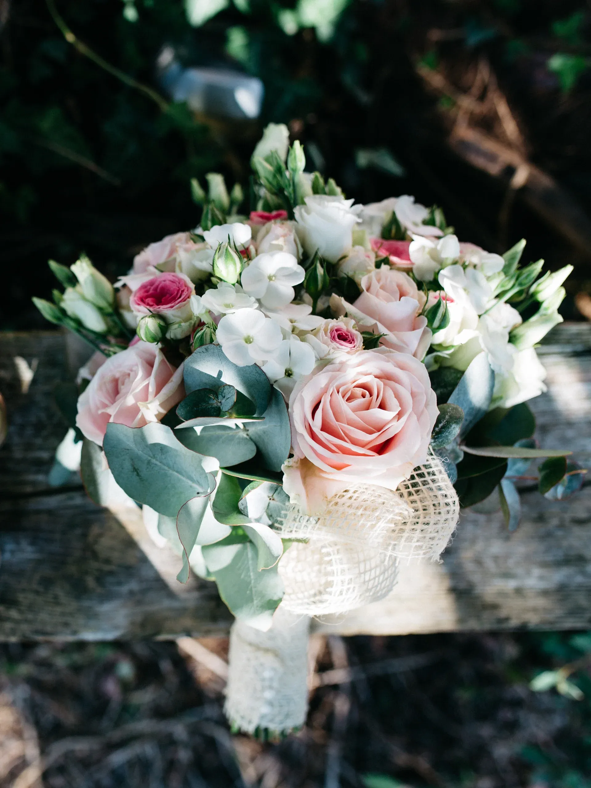 A bridal bouquet of blush roses and white blooms resting on a weathered timber bench, seen from above