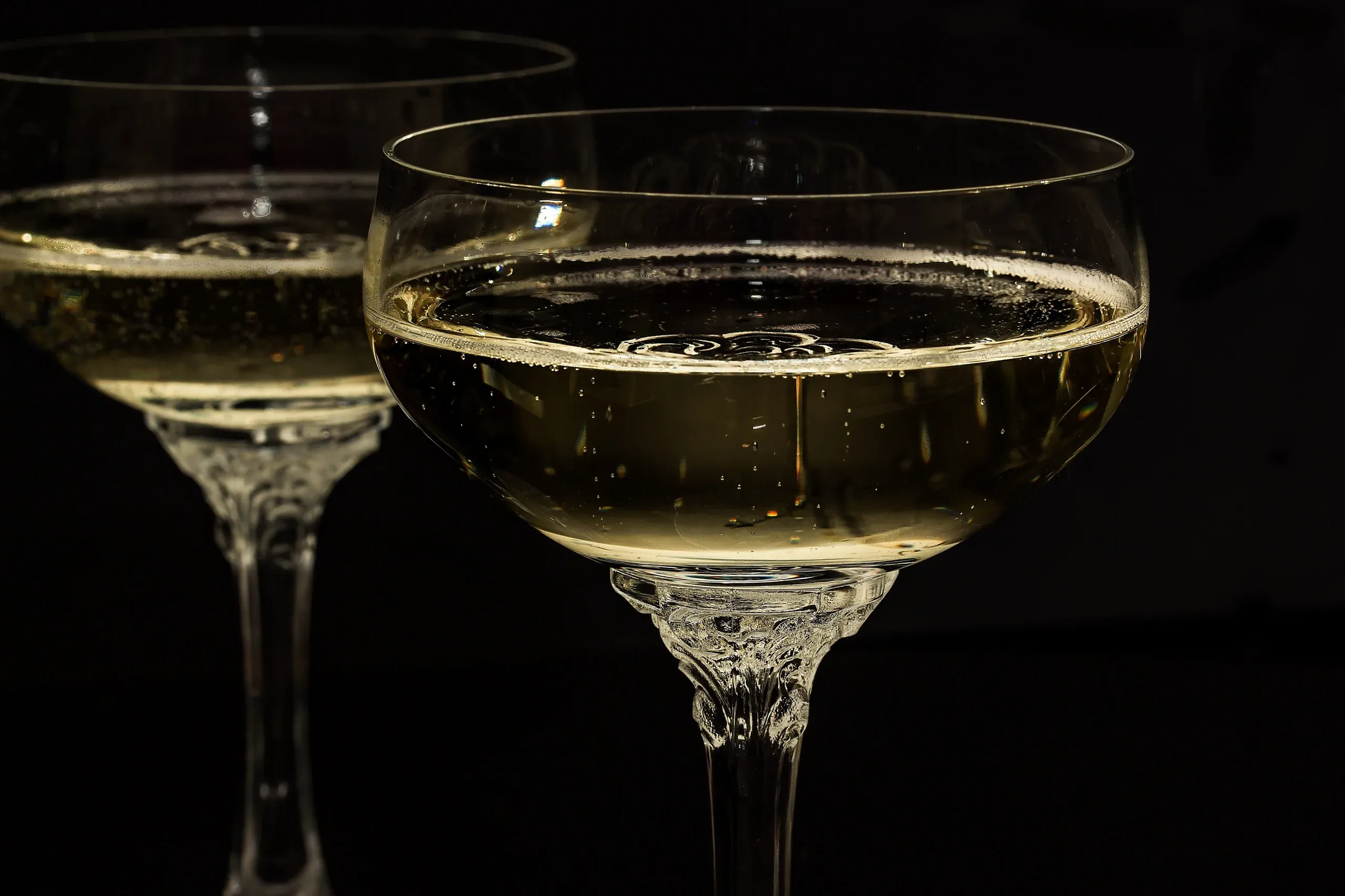 Two coupes of sparkling wine against a dark background