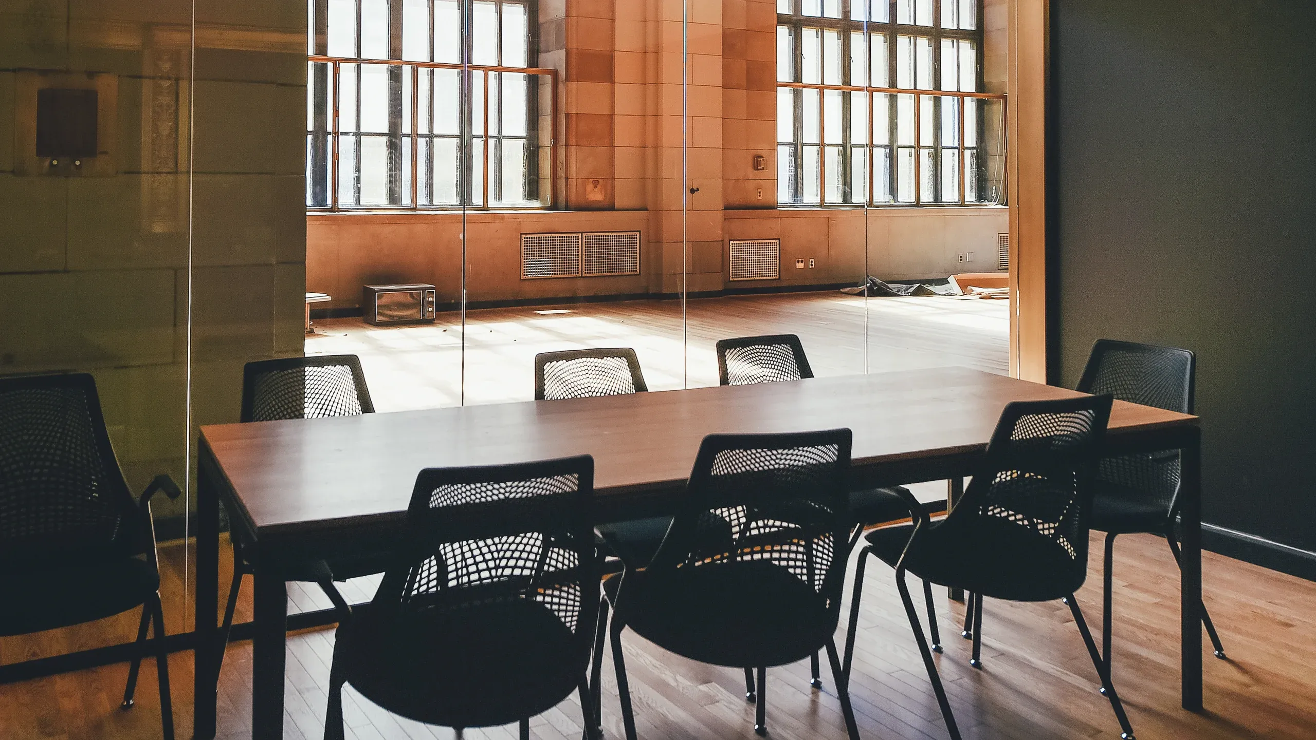 A long meeting table and chairs on timber floorboards, with tall windows in the room beyond