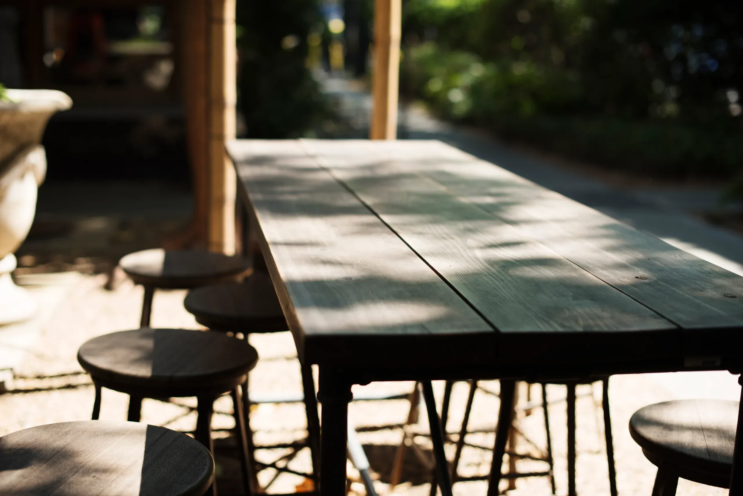 A long timber table and stools under dappled shade in the garden